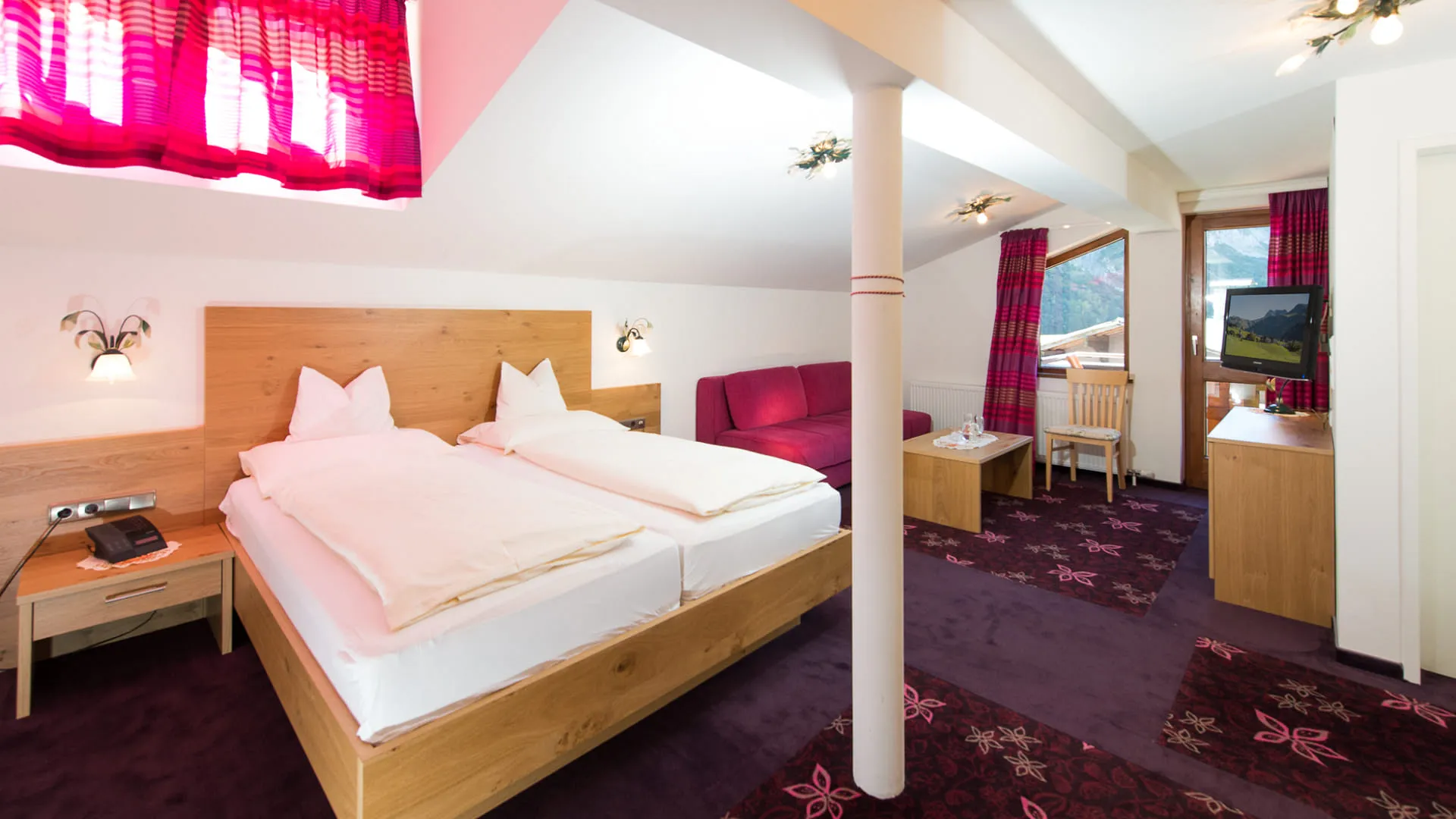 Helle Hotelzimmer mit Doppelbett, TV, und bunten Vorhängen.