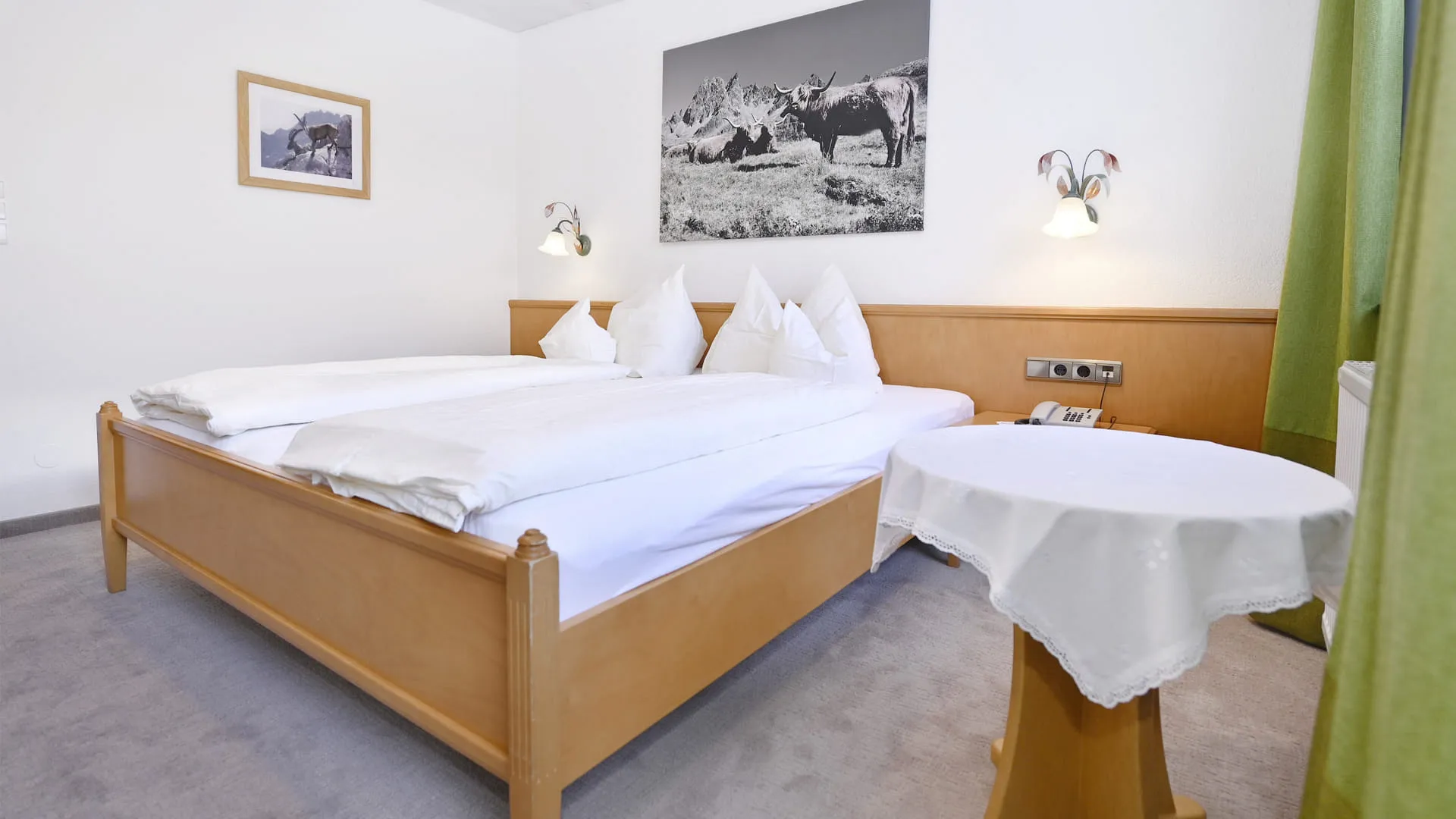 Helles Schlafzimmer mit zwei Betten, Tisch und grünen Vorhängen.