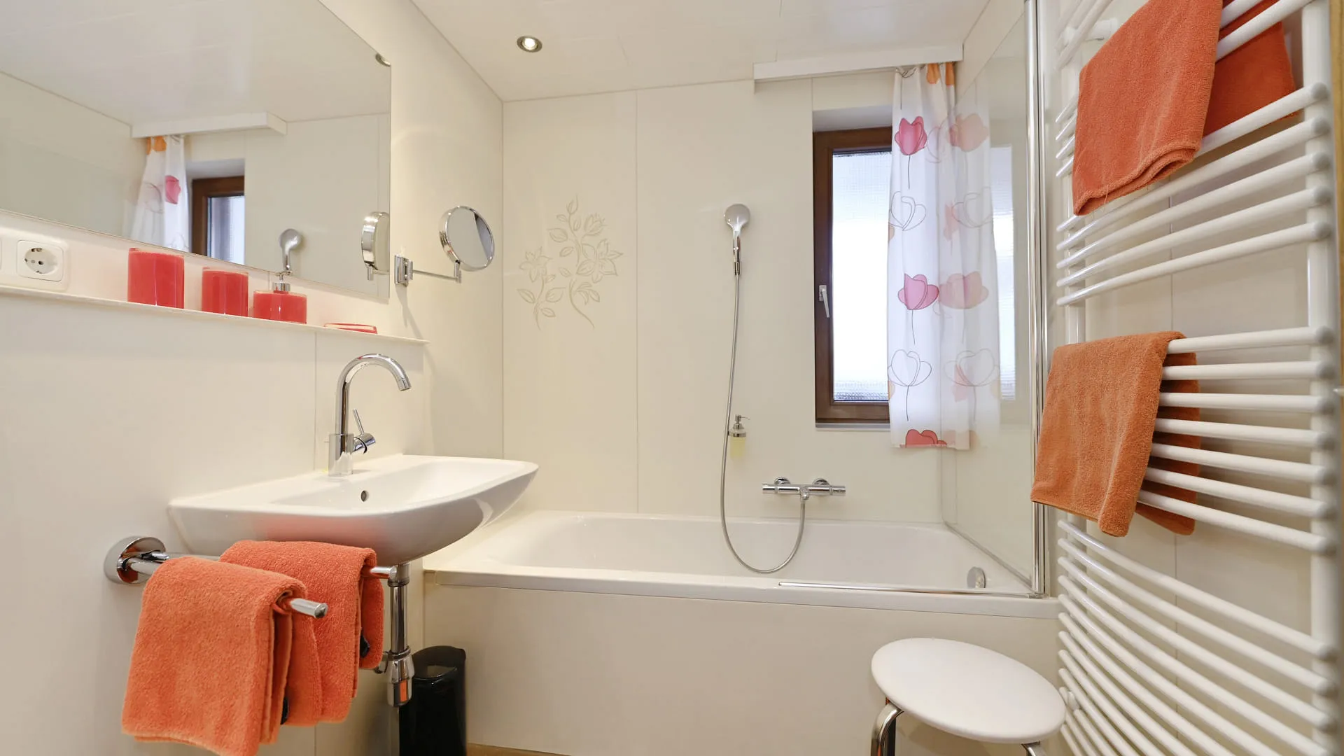 modernes Badezimmer mit Badewanne, Waschbecken, orangefarbenen Handtüchern und Dusche